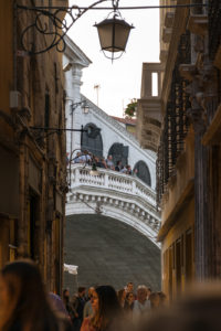 An alley with people and the Rialto Bridge in the end