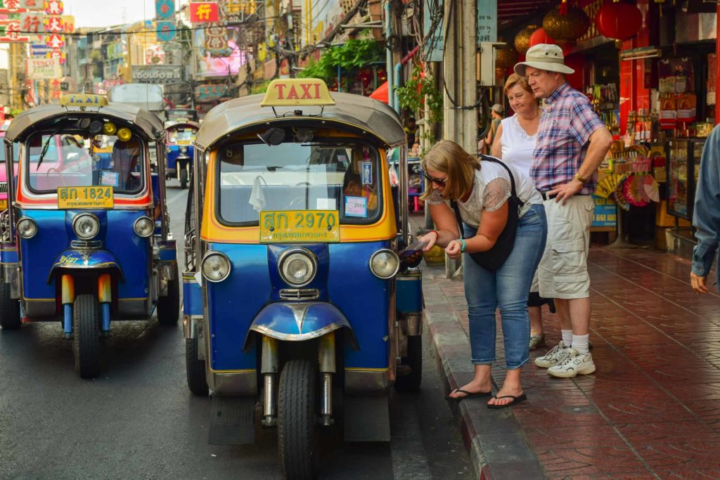 Uma turista com sua família falando com o motorista de um tuktuk no meio do caos de Bangkok