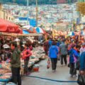 Many people and market stalls in the streets of Busan with many colourful houses in the background on top of the mountain