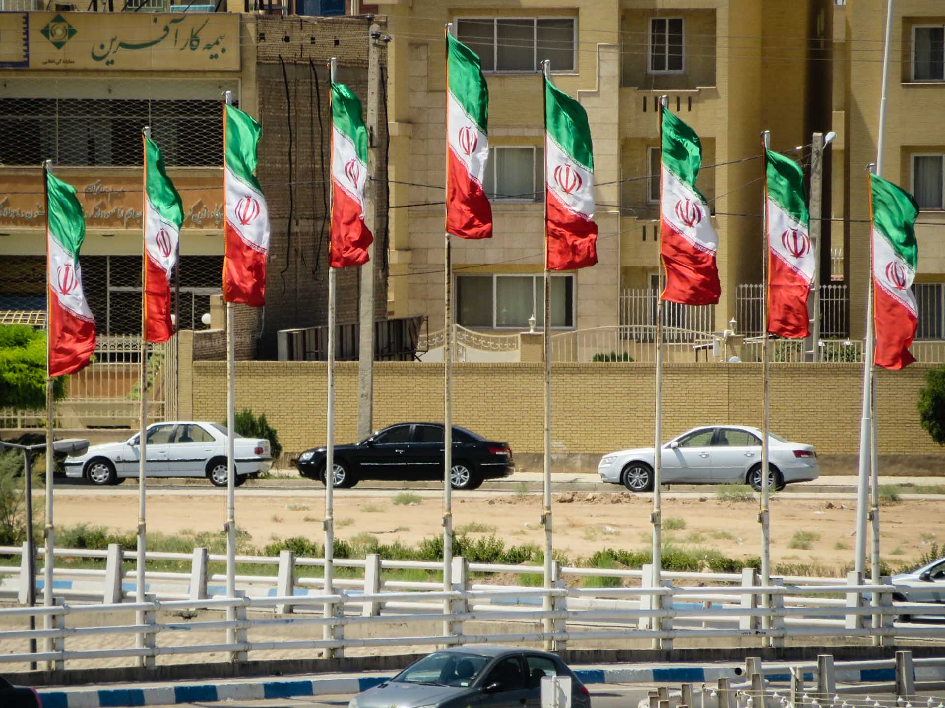 Bandeiras iranianas em mastros pela cidade com carros passando