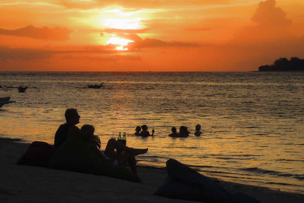O por-do-sol em Gili Air com pessoas nadando no mar e outras sentadas na areia e bebendo