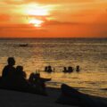 The sunset in Gili air with people swimming in the sea and others sitting in the sand drinking