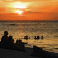 O por-do-sol em Gili Air com pessoas nadando no mar e outras sentadas na areia e bebendo