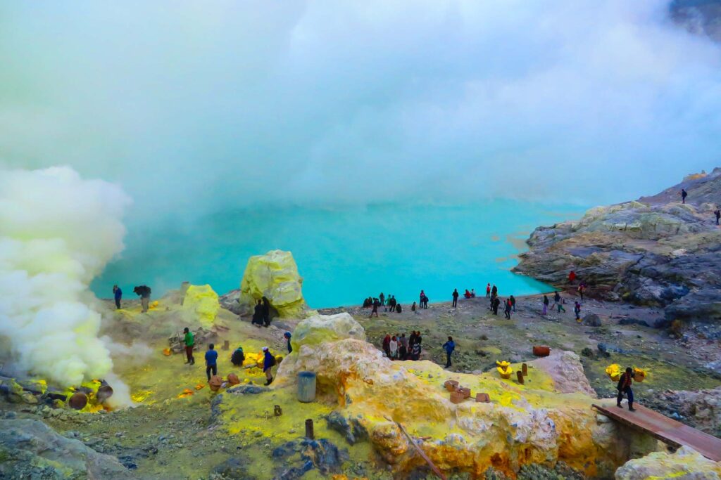 O lago ácido de cor azul turquesa na cratera do vulcão Ijen com muitas pessoas ao redor