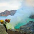 A man carrying sulphur in two baskets on his shoulder up the Ijen volcano with the acid lake in the background