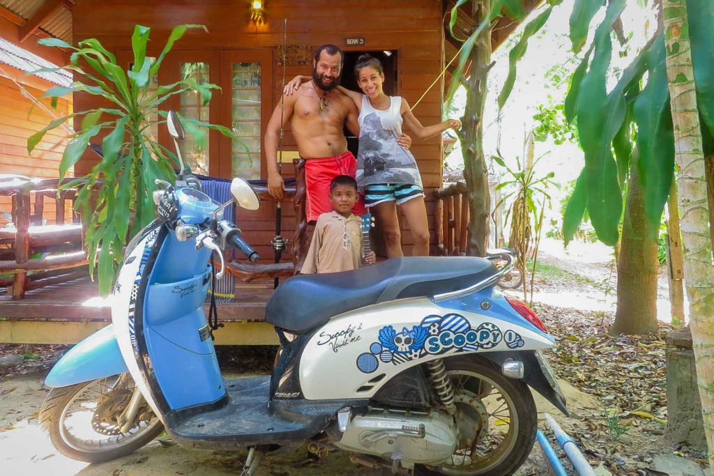 Tiago e Fernanda com uma criança e uma moto na frente do bangalô de Koh Lanta