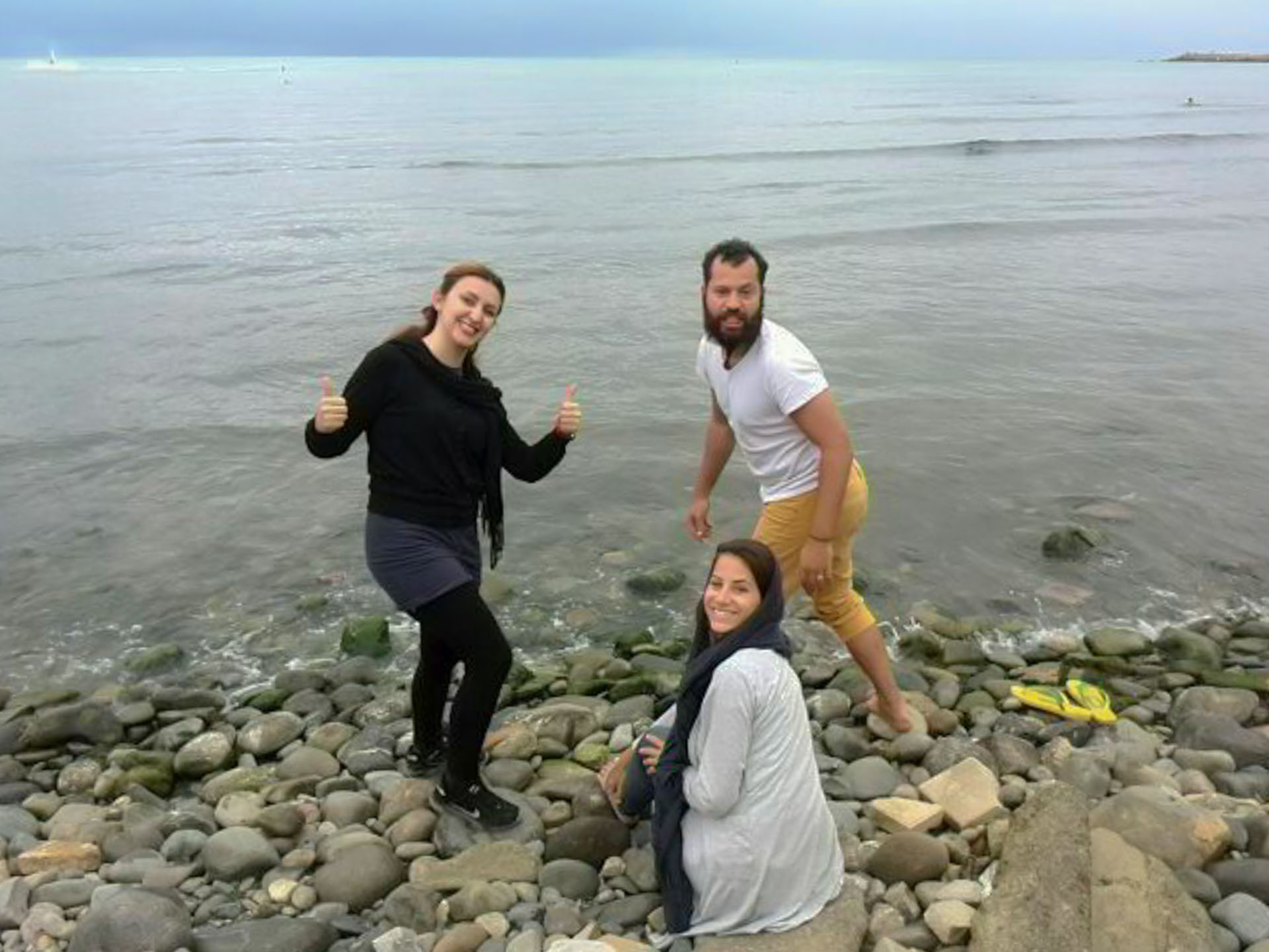 Tiago, Fernanda e sua amiga iraniana na beira no mar negro com chão de pedras