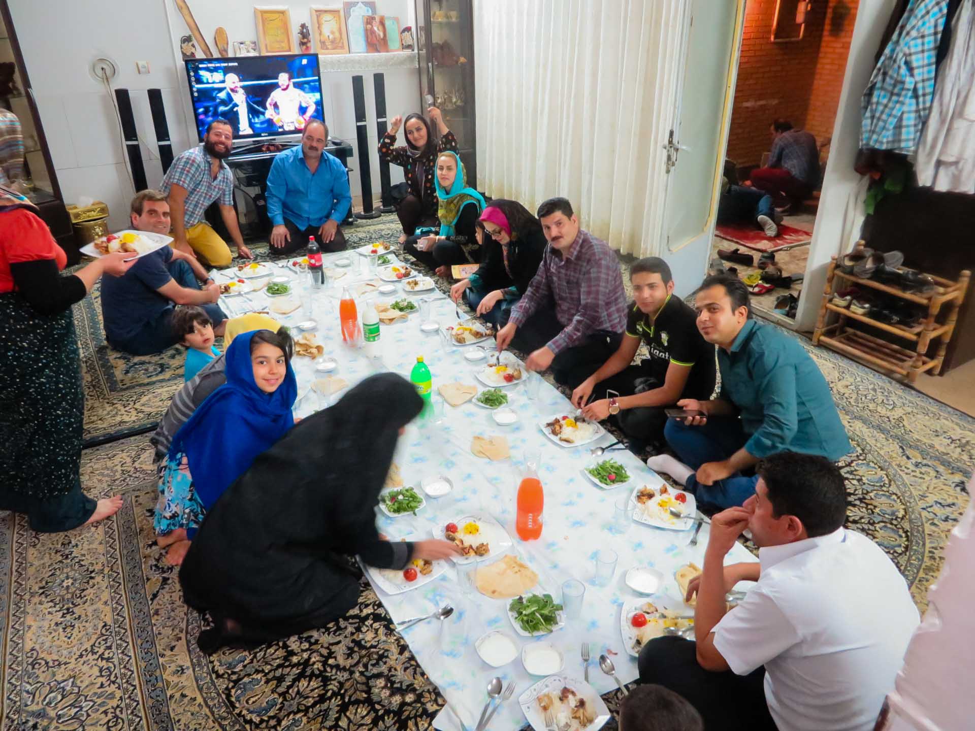 Família iraniana sentada no chão da sala com a mesa posta para jantar