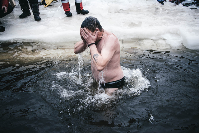 A man diving into a freezing water surrounded by ice in Russia