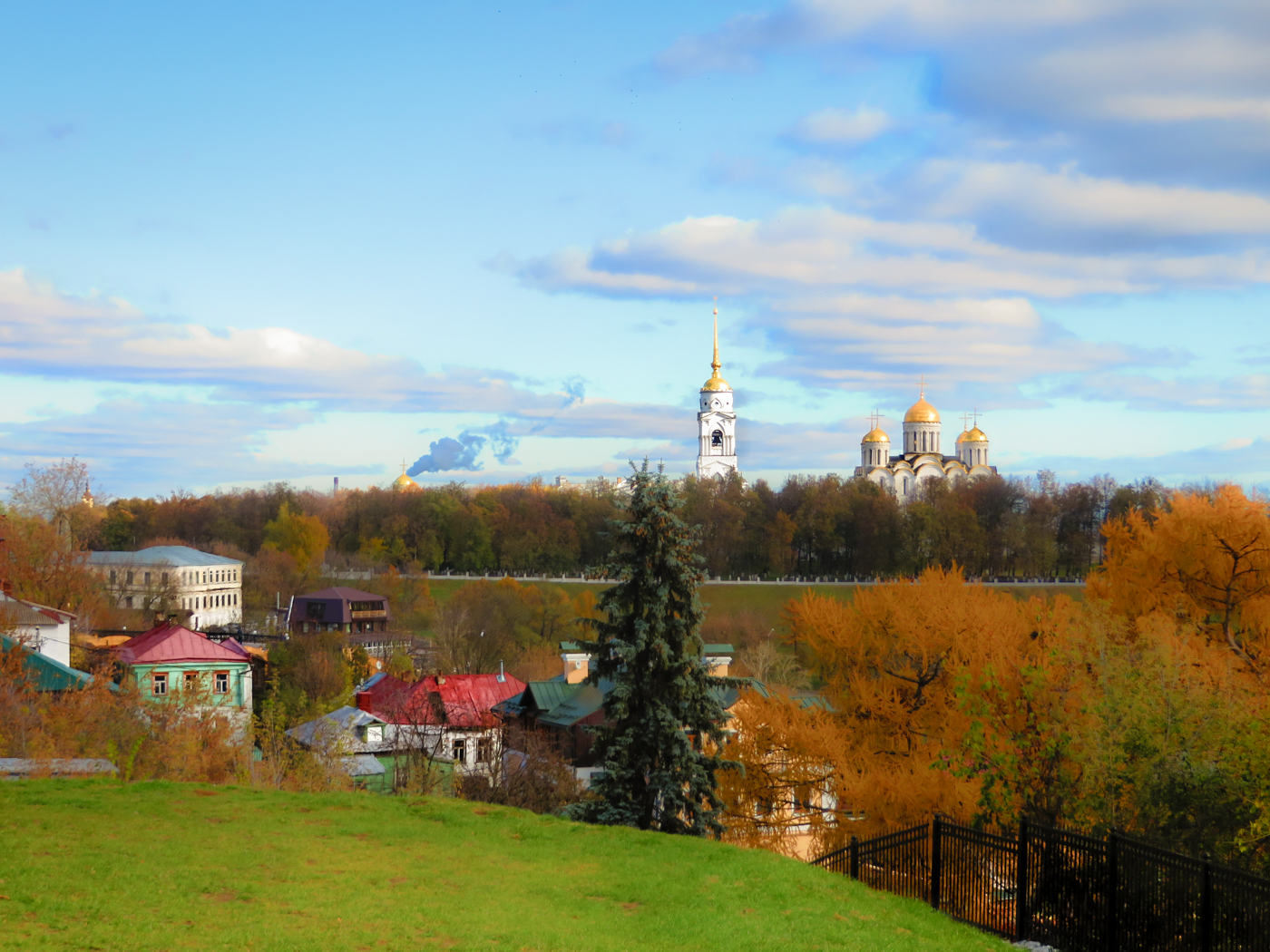 O interior da Russia com algumas casas e uma igreja ortodoxa ao fundo e arvores com cores de outono num dia claro