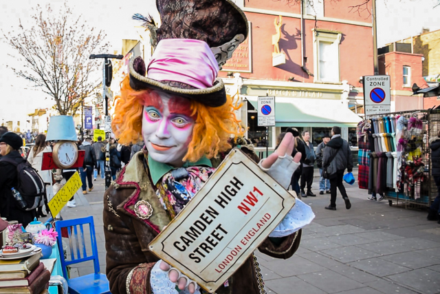 Artista de rua em Camden Town vestido de chapeleiro maluco segurando uma placa de Camden High Street
