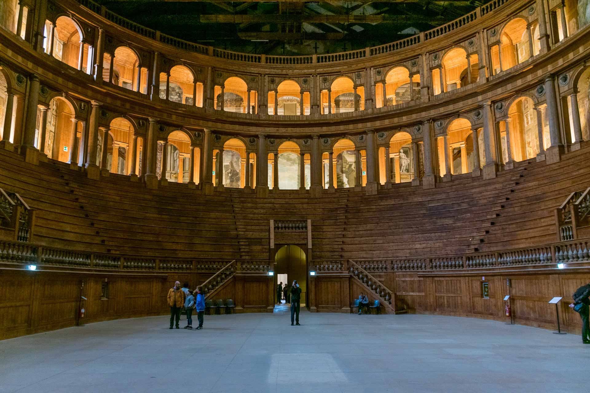 Inside an oval theatre with many seats and a few people taking photos