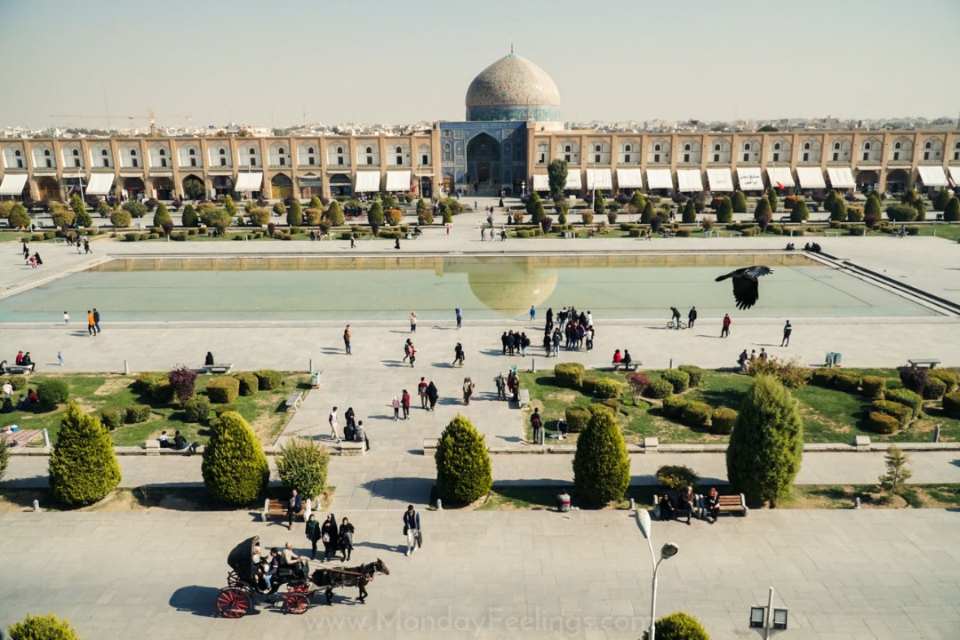 Praça Naqsh-e Jahan em Esfahan com o lago no meio, mesquita ao fundo pessoas andando, carroças e passaros voando