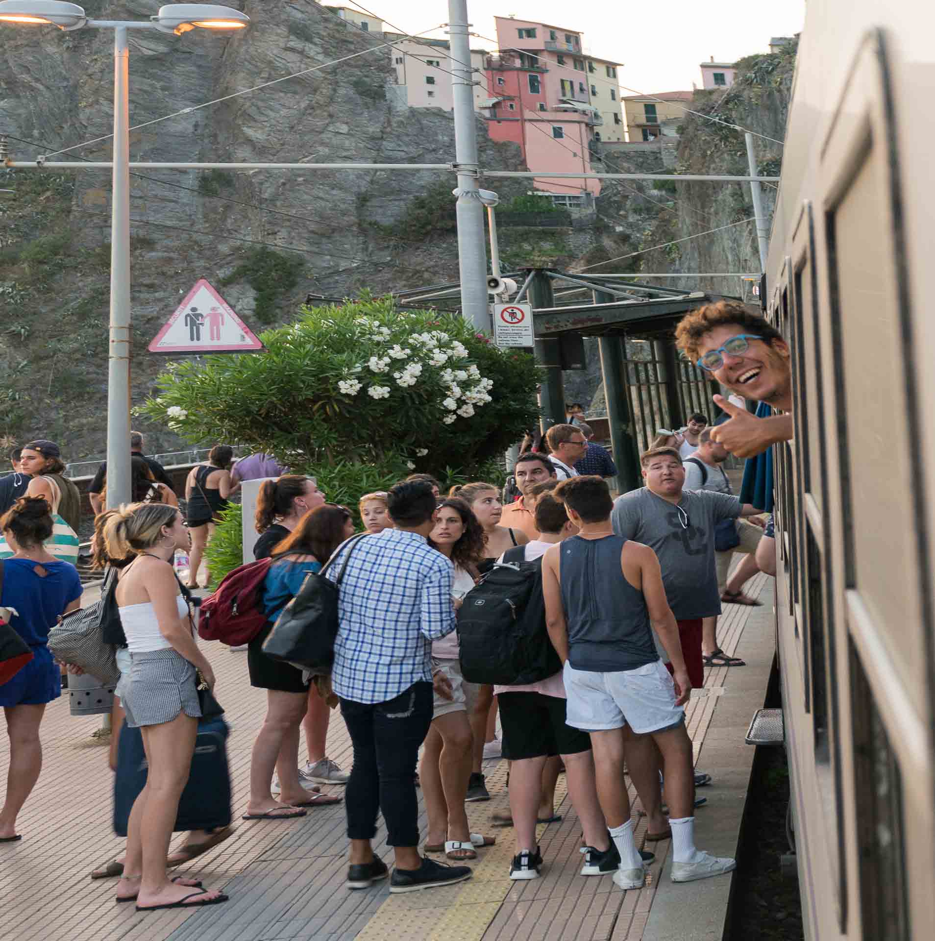 A guy sticking his head out of the train window with the train stopped at the platform and people getting in