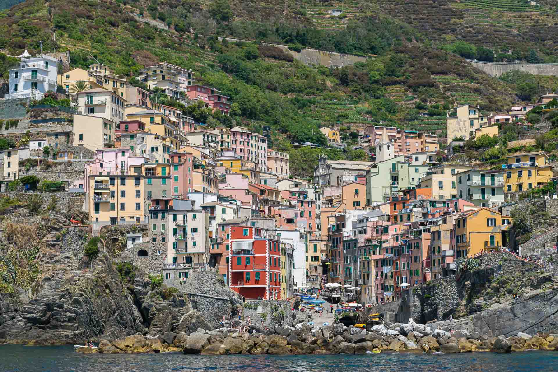 A vila de Riomaggiore vista do mar com suas casas em cada lado da montanha descendo em forma de V até a praia