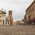 A large square in Mantua Italy with a church in the end on one side and the road and a palace on the other with a tower in between