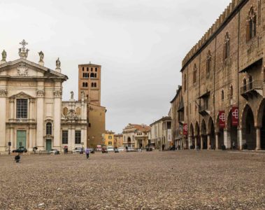 A large square in Mantua Italy with a church in the end on one side and the road and a palace on the other with a tower in between