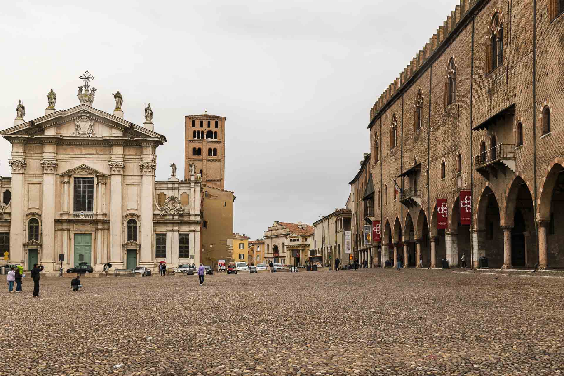 A large square in Mantua Italy with a church in the end on one side and the road and a palace on the other with a tower in between