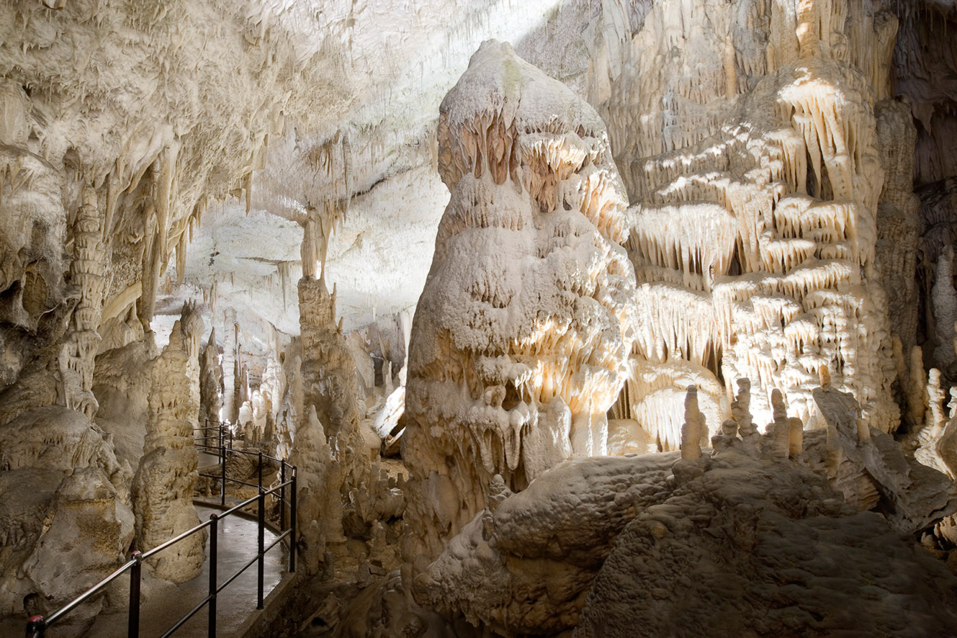 The large white hall inside Postojna Cave with a gigantic rock formation near where people pass