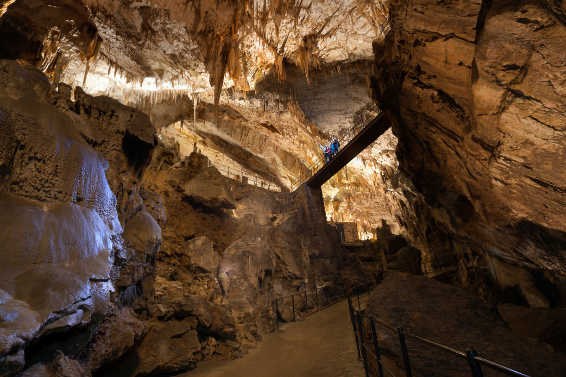 Uma ponte no alto conectando duas rochas dentro da caverna de Postojna com pessoas em cima da ponte