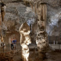 Uma grande formação rochosa dentro da caverna de Postojna com duas pessoas olhando e apontando