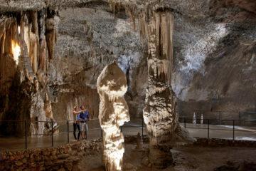 Uma grande formação rochosa dentro da caverna de Postojna com duas pessoas olhando e apontando