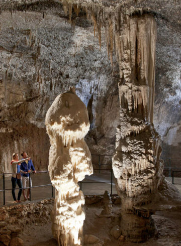 A large stalagmite inside Postojna Cave and other stalactites and a couple observing them