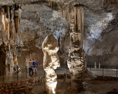 Uma grande formação rochosa dentro da caverna de Postojna com duas pessoas olhando e apontando