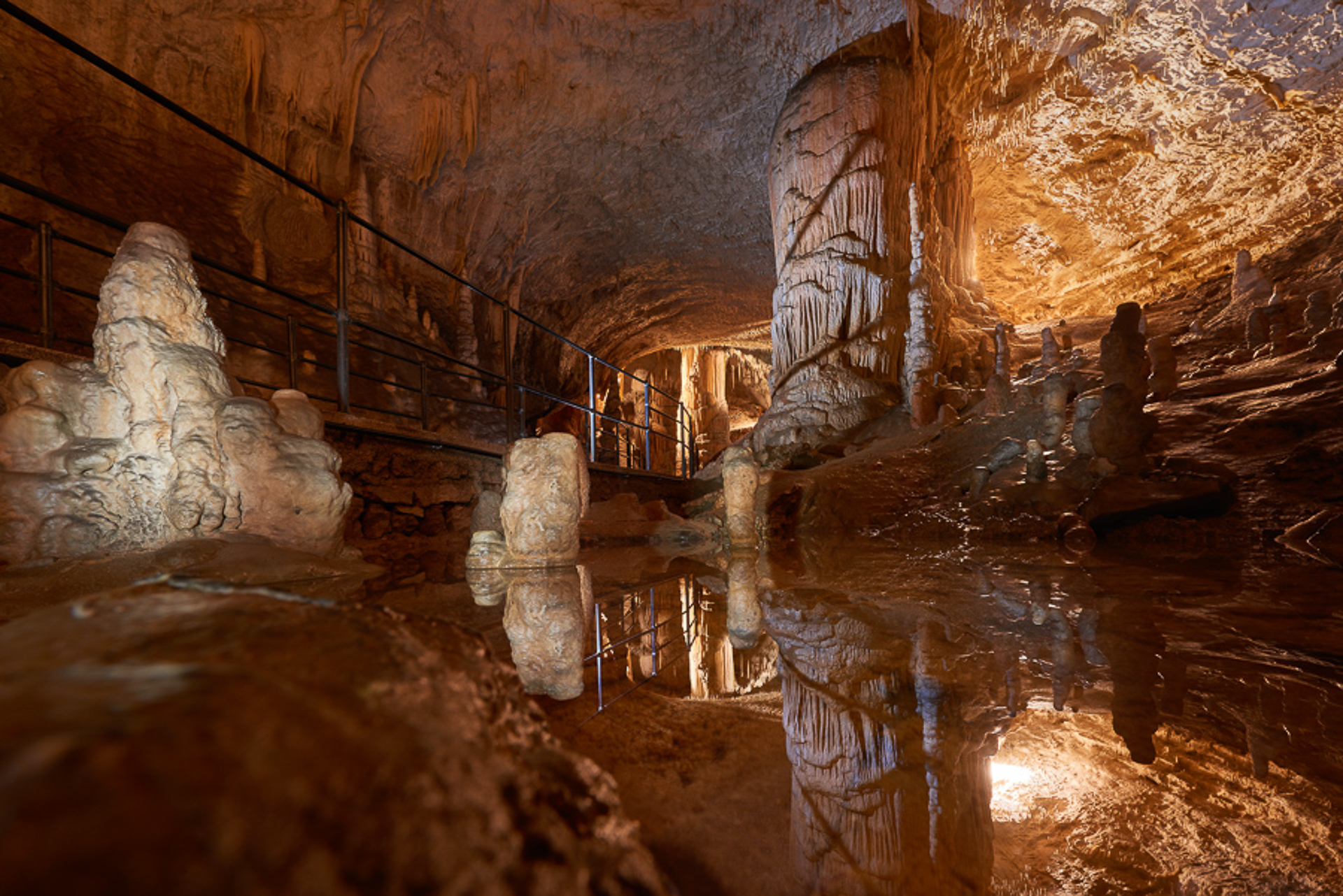 Dentro da caverna de Postojna refletida por uma lago ao lado de onde passam os turistas