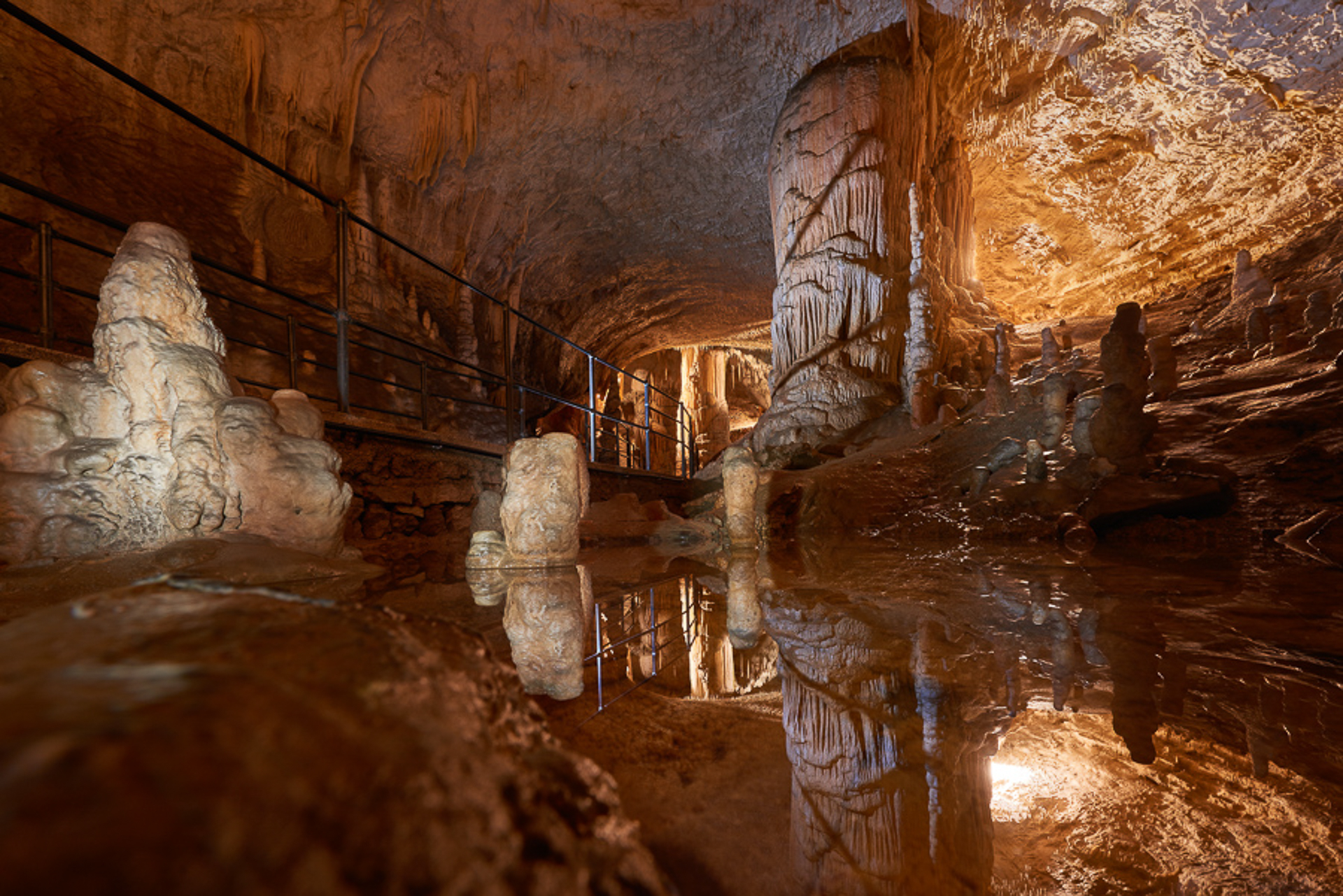 Inside Postojna Cave with a little lake reflecting the cave and the passage for the tour