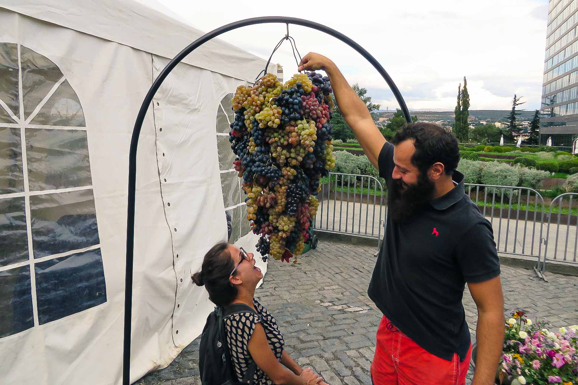 Tiago holding a massive grape bunch and Fernanda ready to eat some