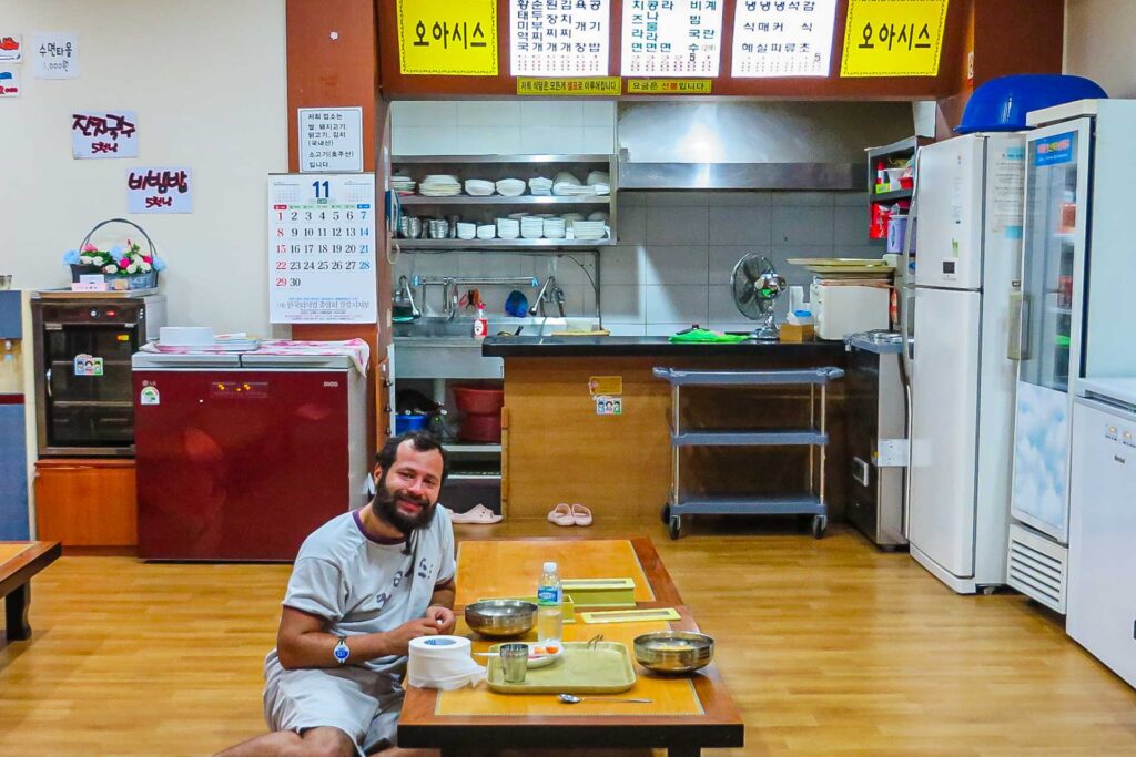 Tiago sentado no chão na mesa de um restaurante dentro da sauna coreana