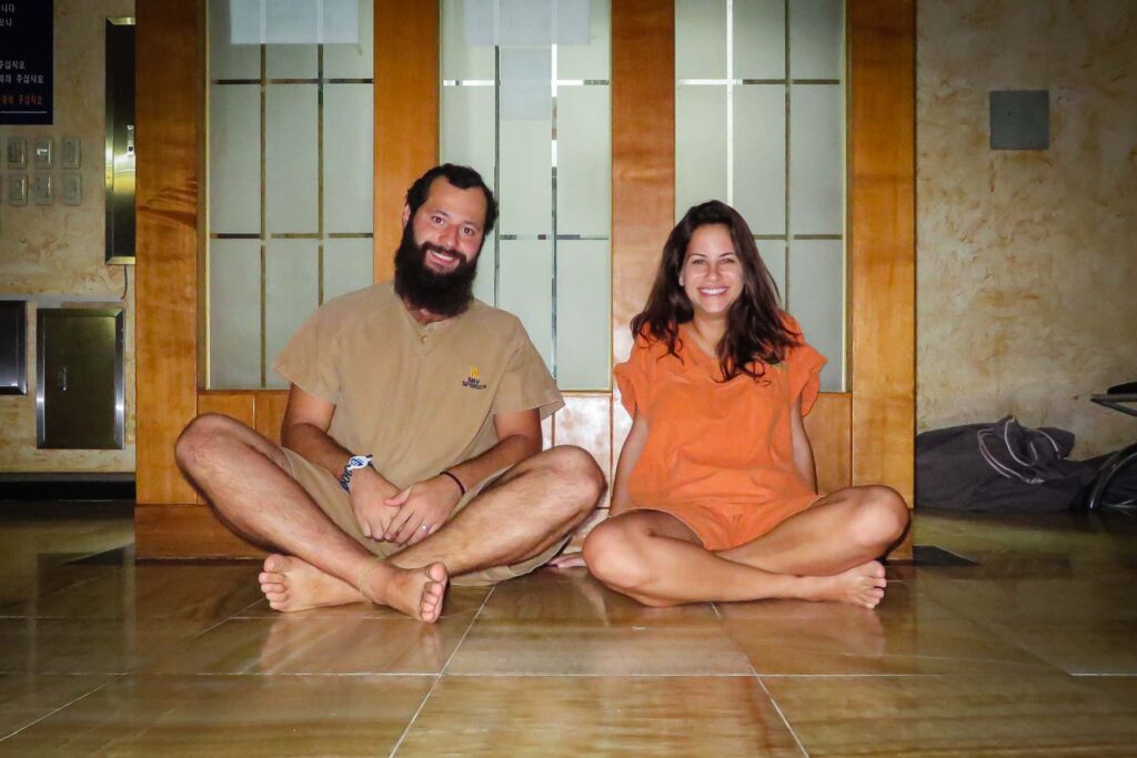 Tiago e Fernanda sentados de perna cruzadas em uma Jjimjilbang