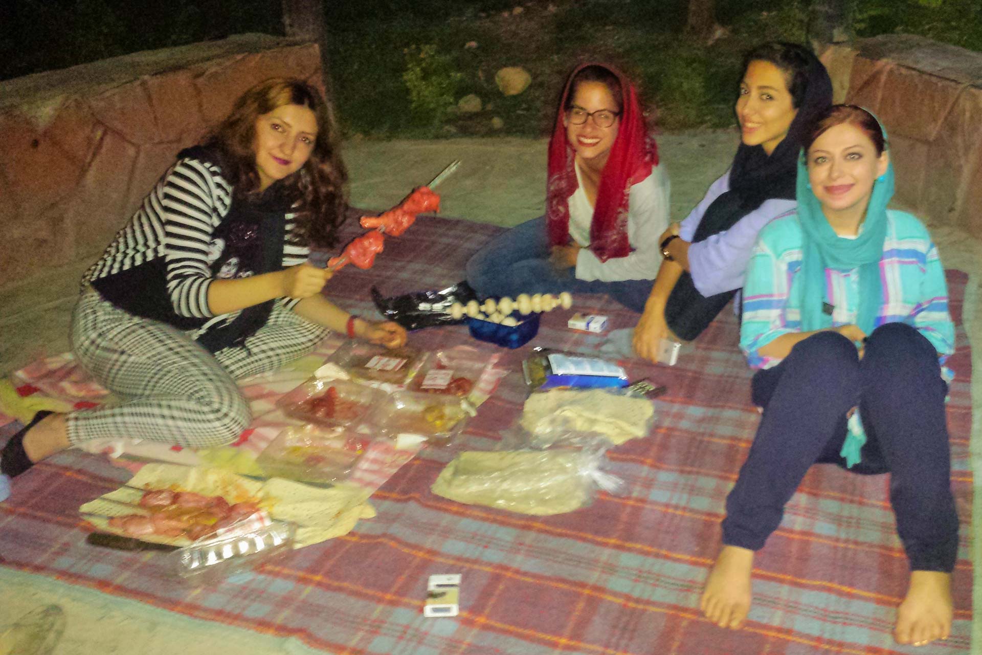 Quatro mulheres sentadas no chão fazendo picnic no parque de Teerã a noite