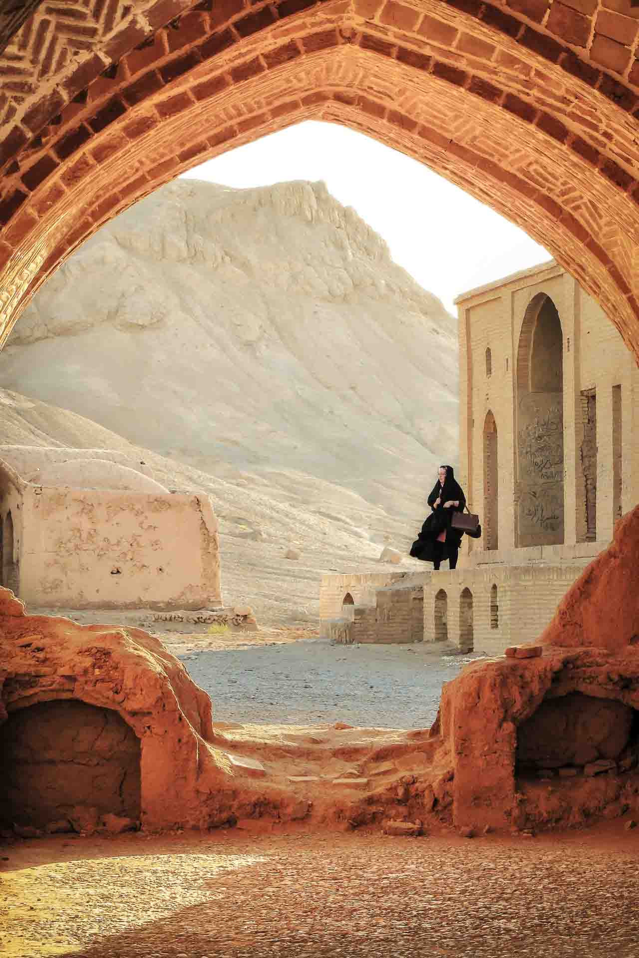 Woman walking in the distance view through a large passage way with a mountain in the background