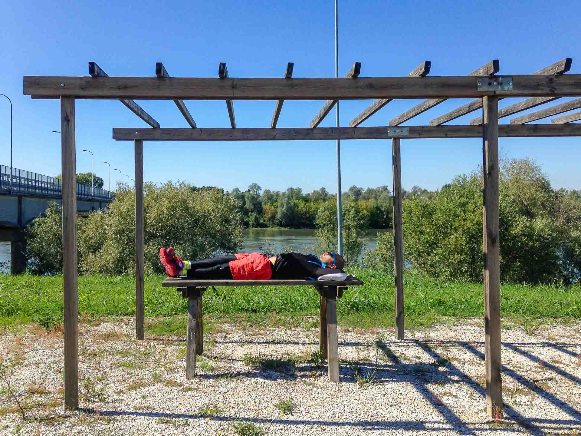 Tiago laying down on a bench by the river Po in Italy in a Eurovelo in Europe