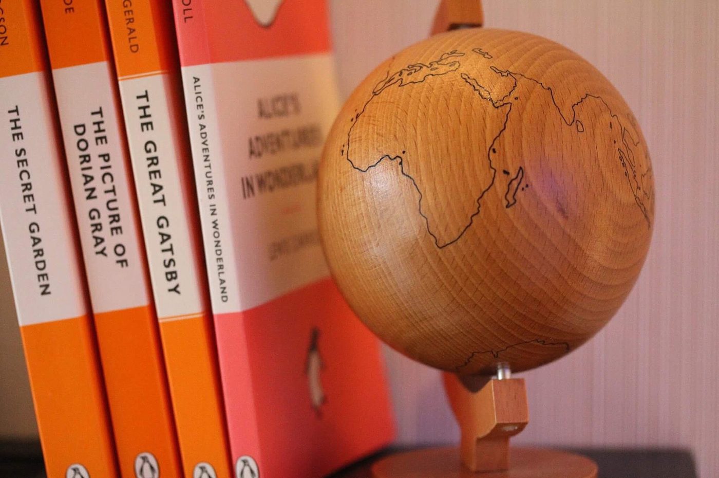 four books on a shelf near a wooden globe