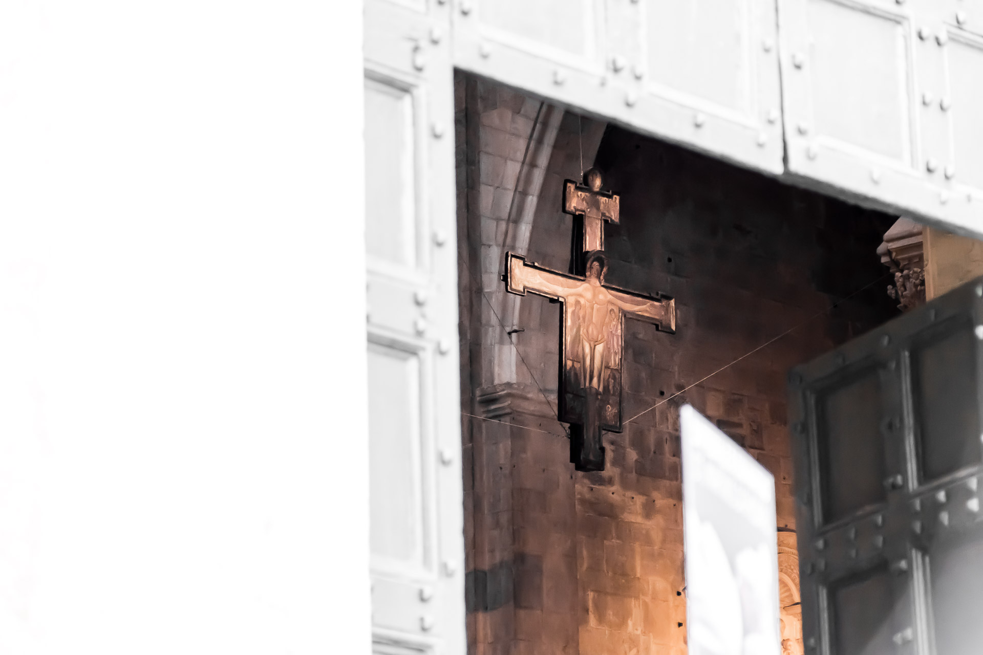 The upper corner of the entrance of a church with a large cross hang inside the Duomo di Lucca