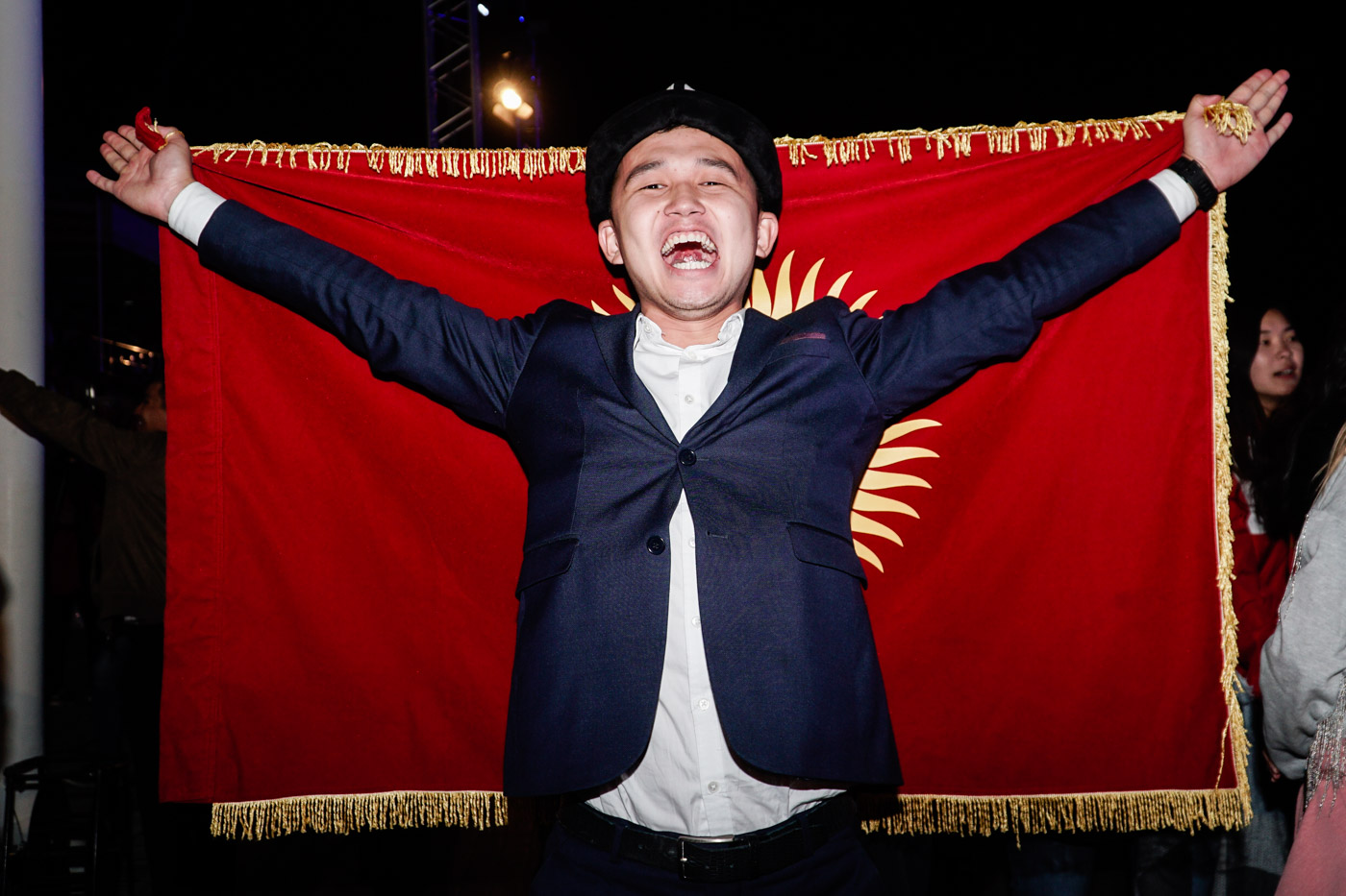a man smiling while holding the flag of kyrgyzstan at the world nomads competition