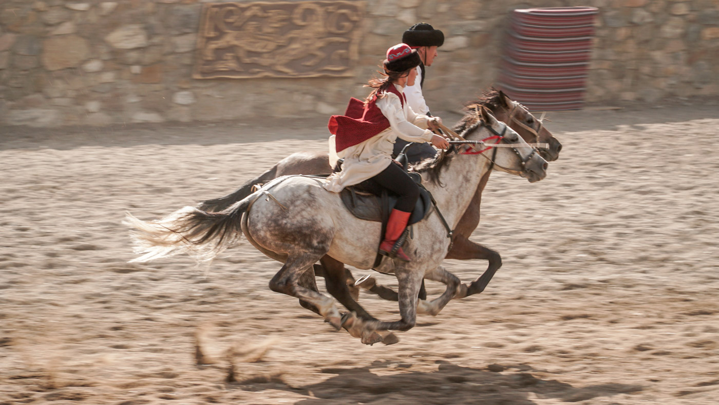 A man and a woman riding a horse synchronised when both horses are in the air