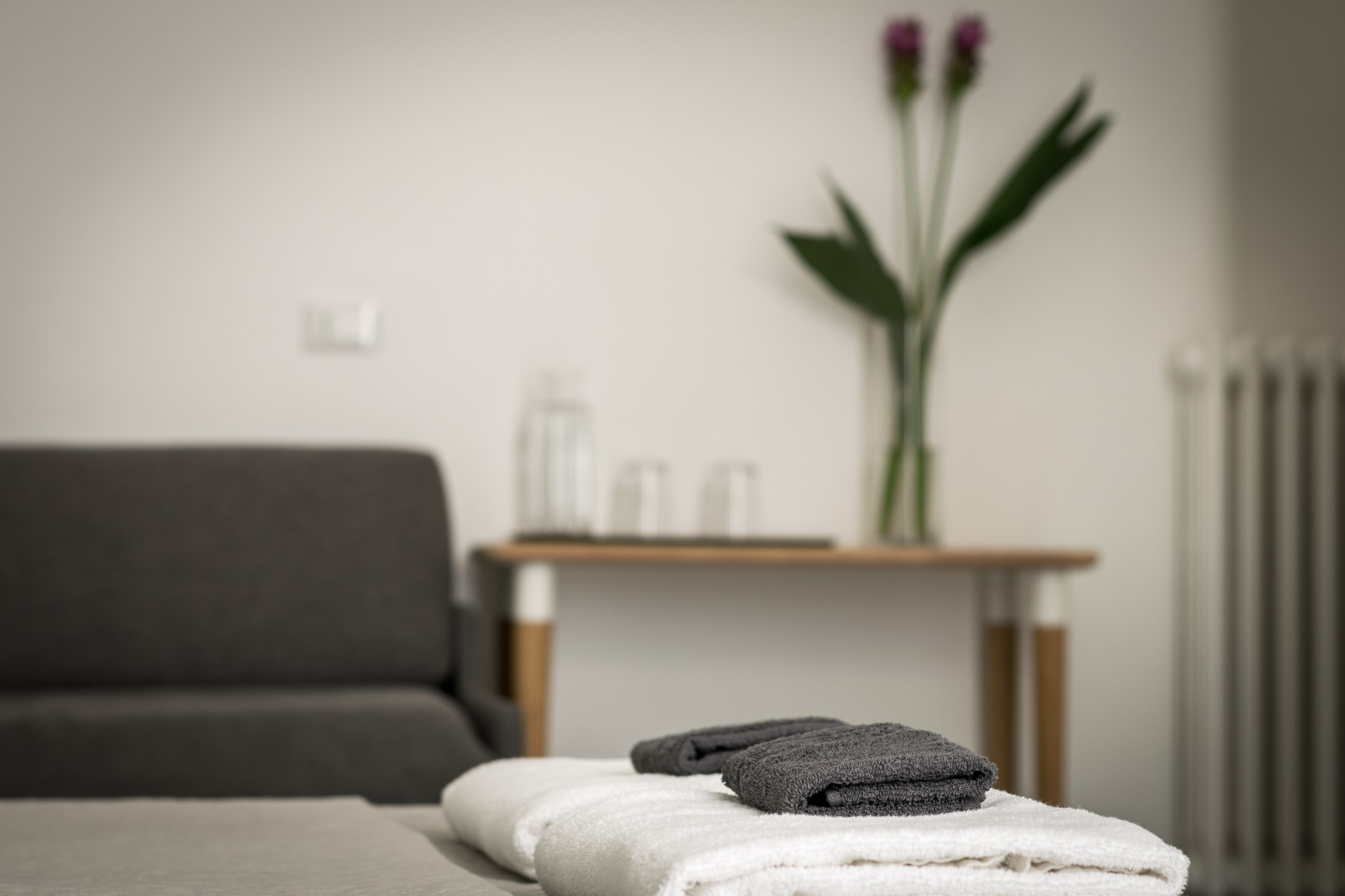 details of the folded towels on top of the bed with a vase of flower not focused in the back