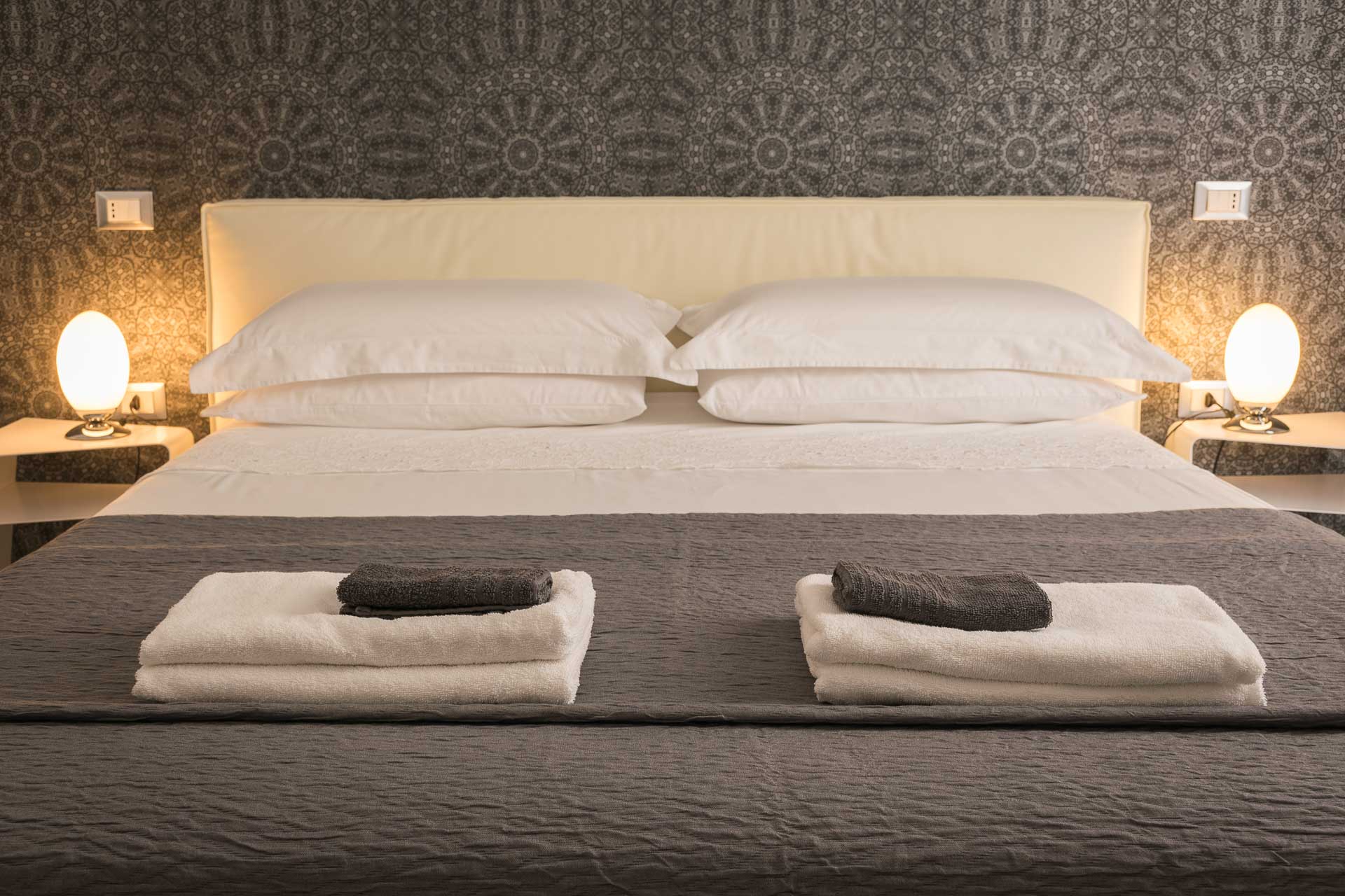 a bed with folded towels on top and warm lights on both bedsides