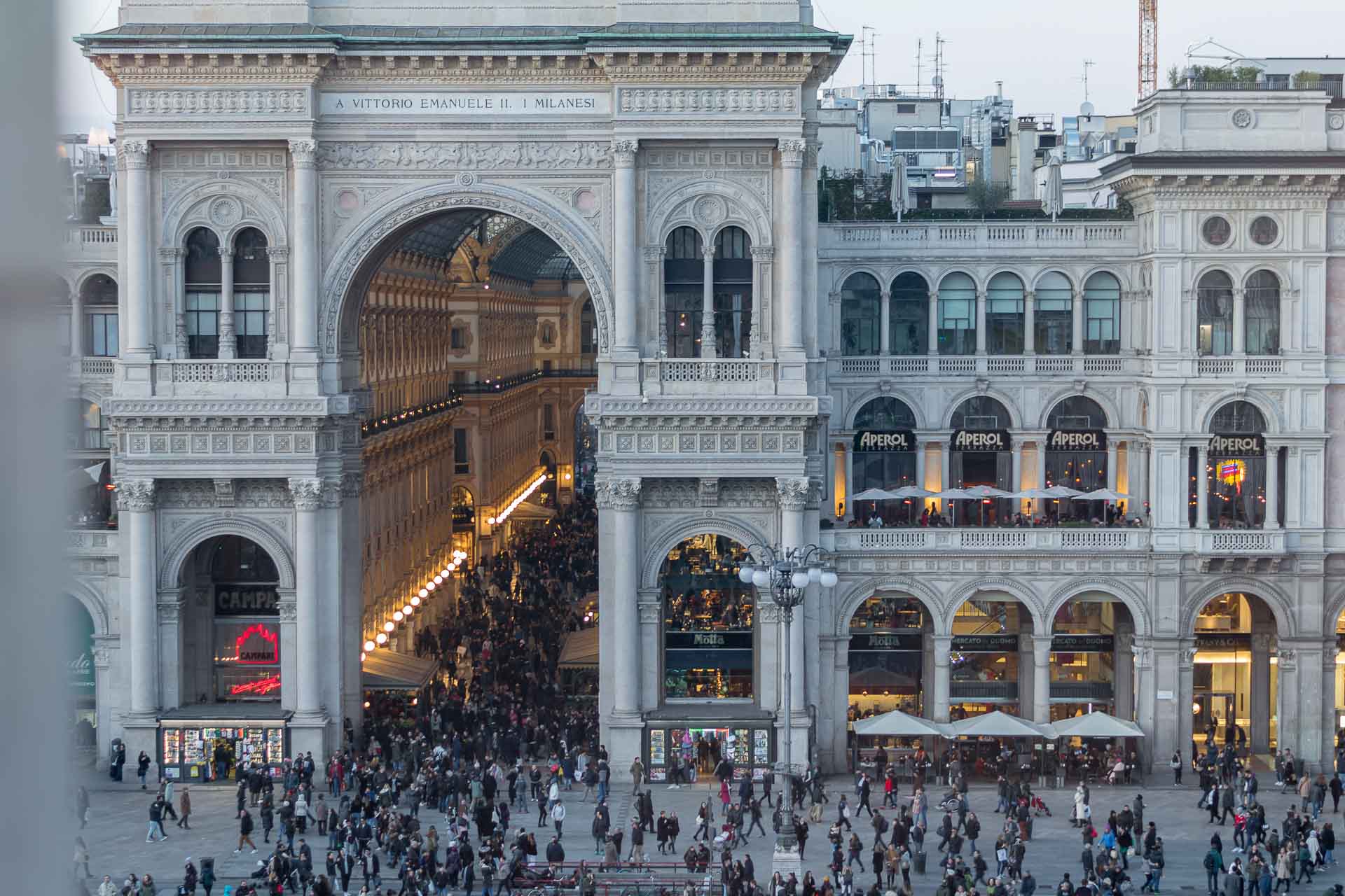 Vista da galeria Vittorio Emanuele II cheia de pessoas e uma entrada enorme em arco