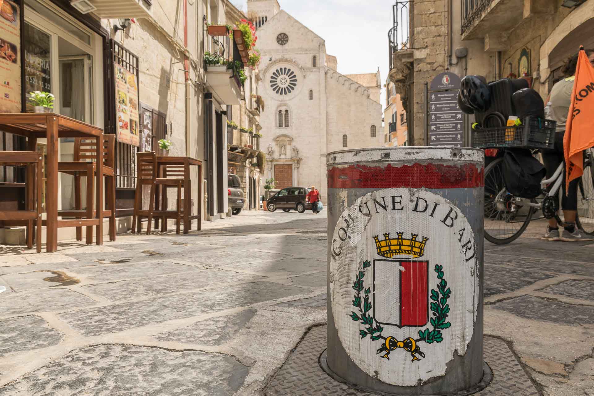 uma rua de bari com a igreja matriz ao fundo com um sinal da comune mostrando que carro não passa