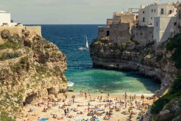 A crowded small beach in between rocks of Polignano A Mare