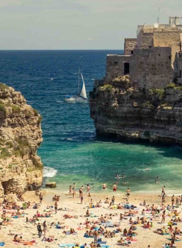 A crowded small beach in between rocks of Polignano A Mare