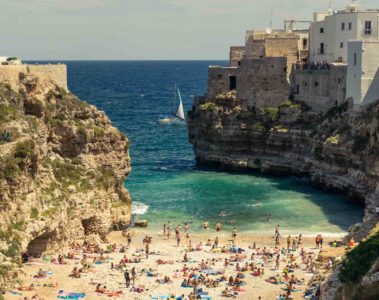 A crowded small beach in between rocks of Polignano A Mare