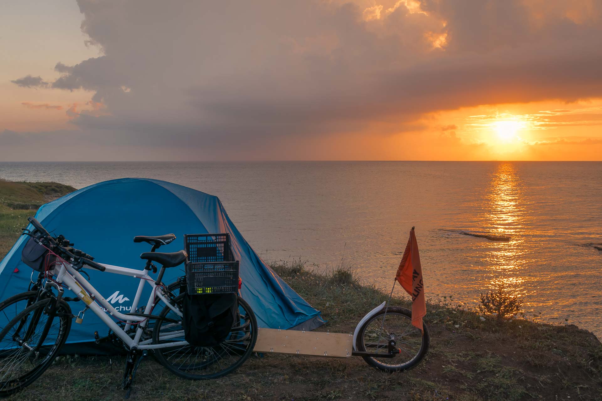 A bike near the camping tent on top of the cliff with the sunset