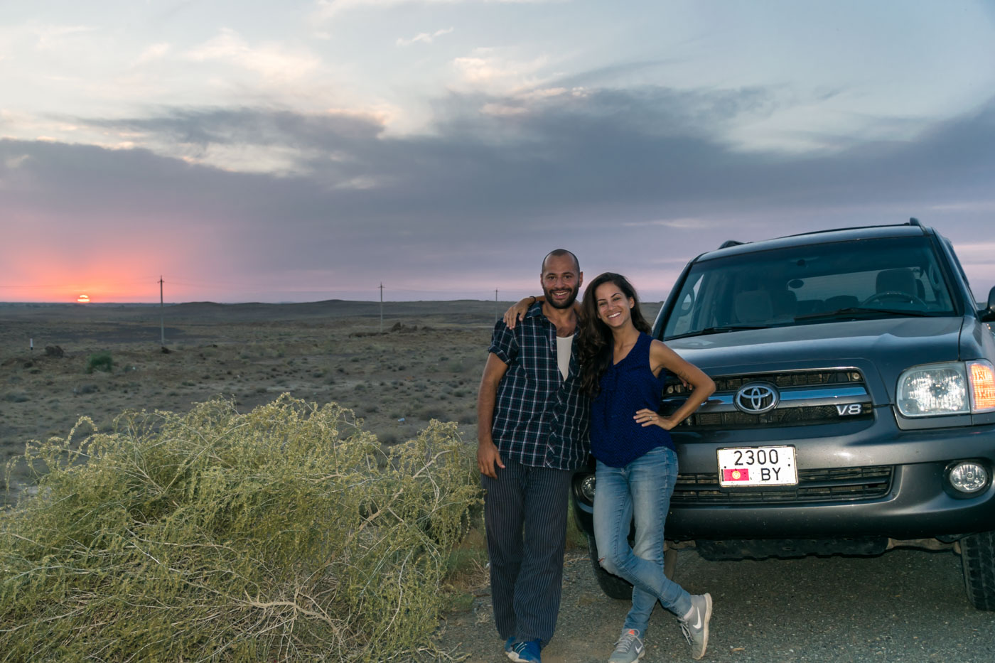 Tiago and Fernanda in front of the car in Kyrgyzstan with the sun setting in the background