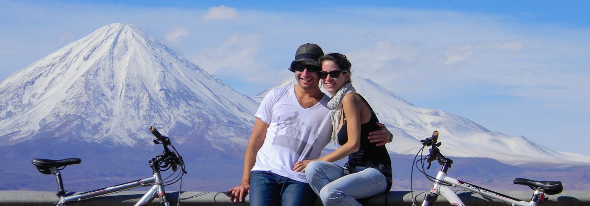 Tiago and Fernanda cycling in Atacama, Chile, with snowed peak mountains in the back